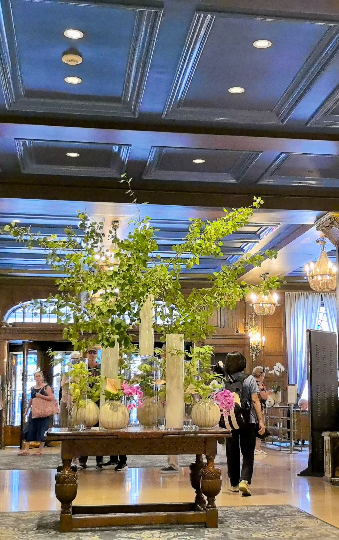 The same floral arrangement photographed from below, with the deep blue coffered ceiling and chandeliers filling the upper half of the frame.